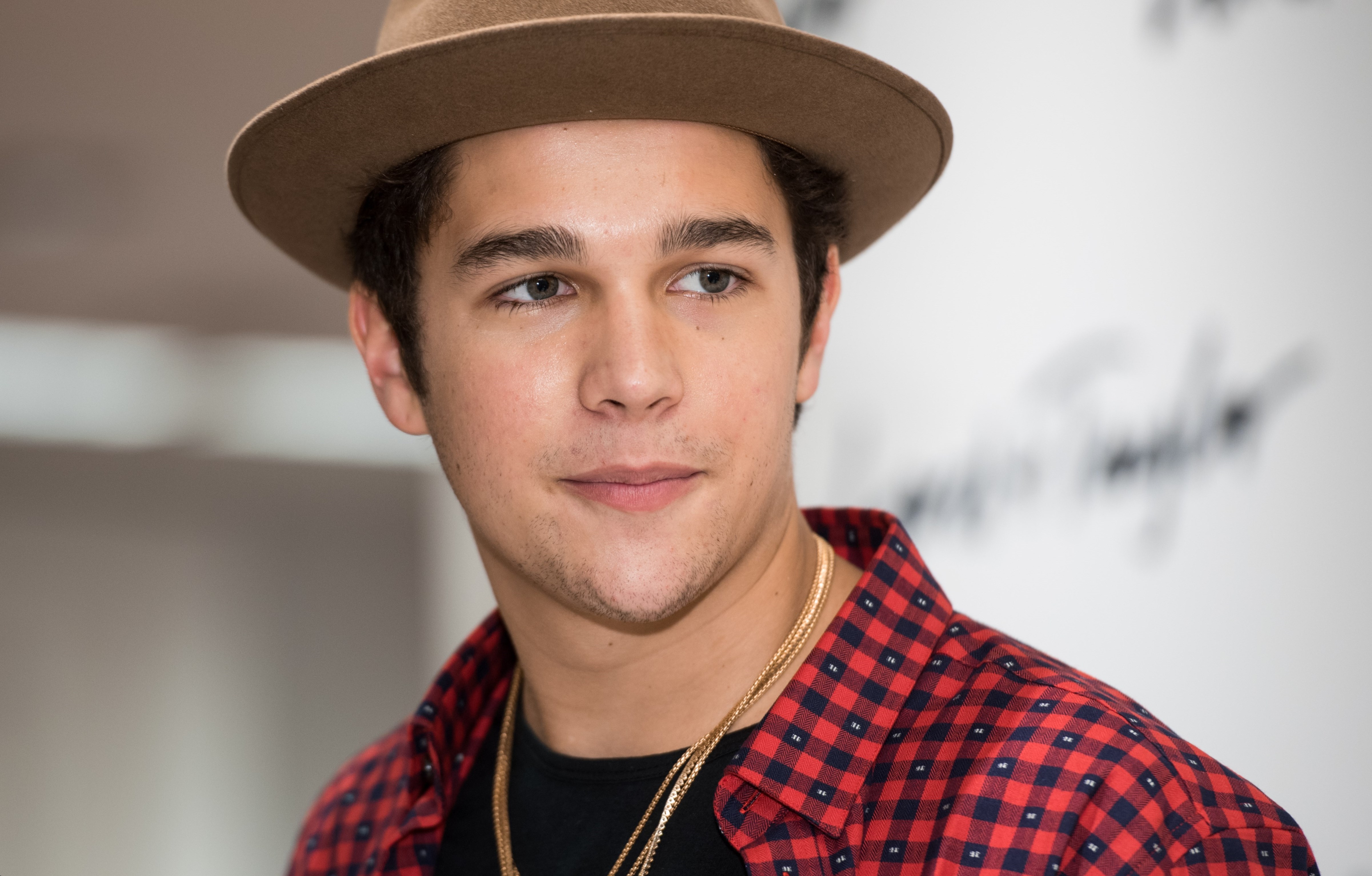 Austin Mahone wearing a red checkered shirt and a brown cap