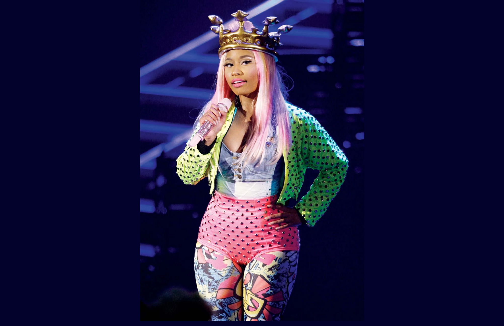 Nicki Minaj performs at a concert while wearing a crown, placing her hands on her waist, and holding a microphone