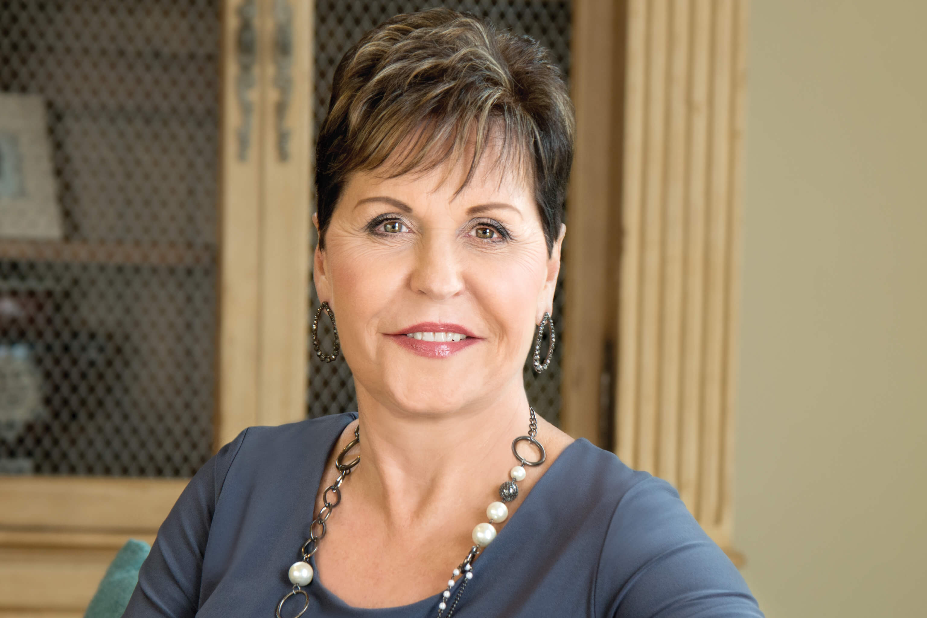 Joyce Meyer in a blue shirt wearing a necklace and earrings