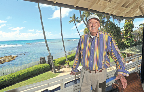 Jim Nabors in striped long sleeve shirt and cap standing at the balcony of his beach house 