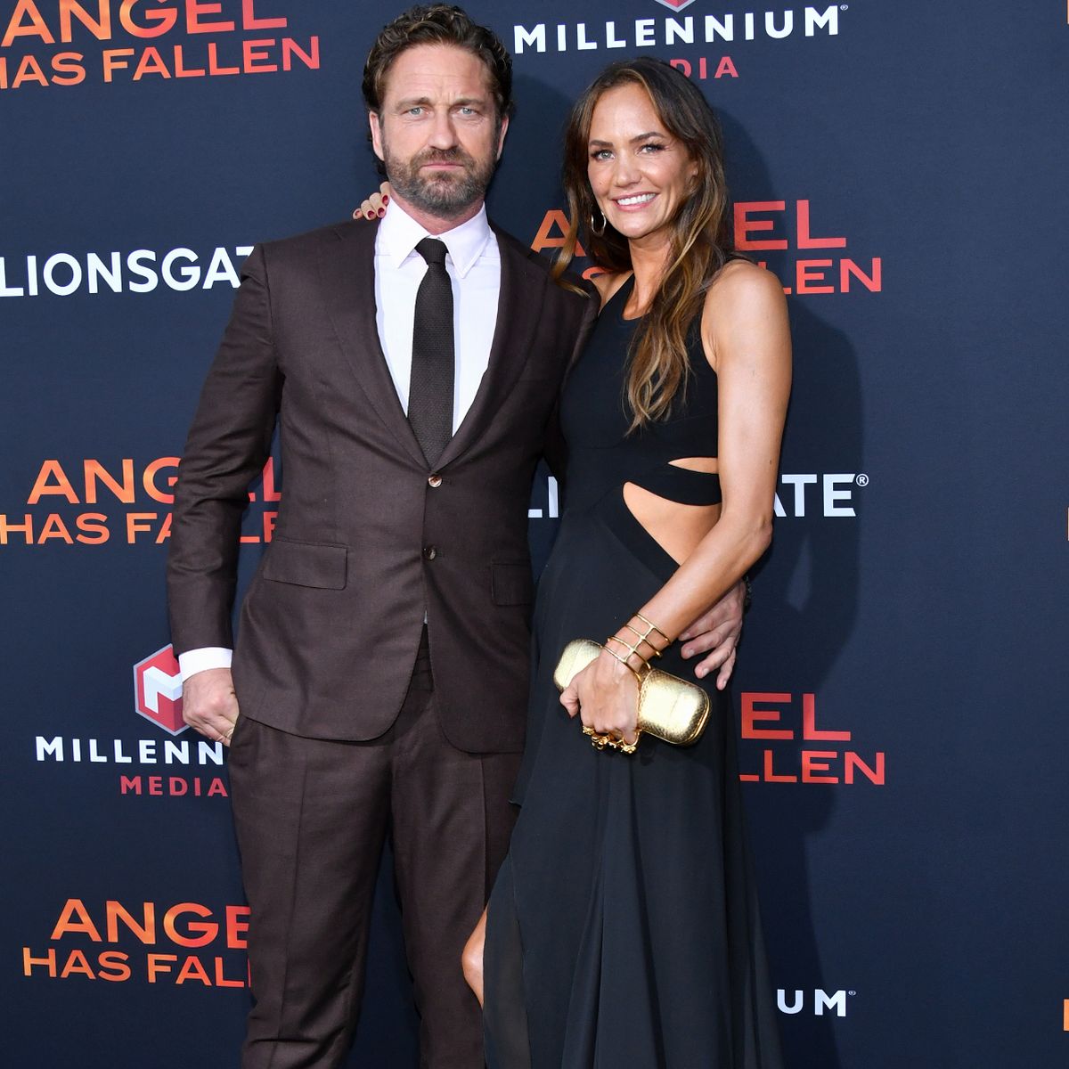 Gerard Butler wearing a black suit and holding his wife by the waist