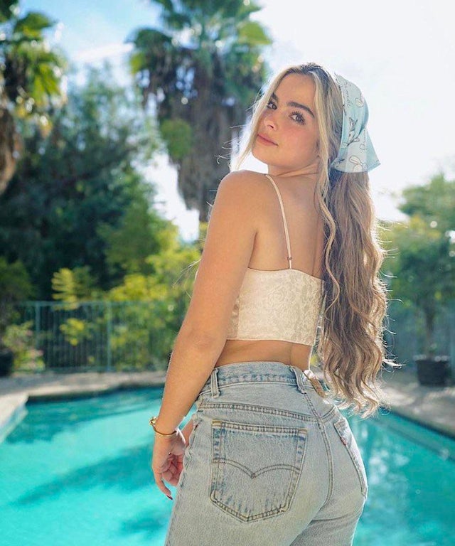 Addison Rae wearing crop top and jeans, and posing beside the swimming pool