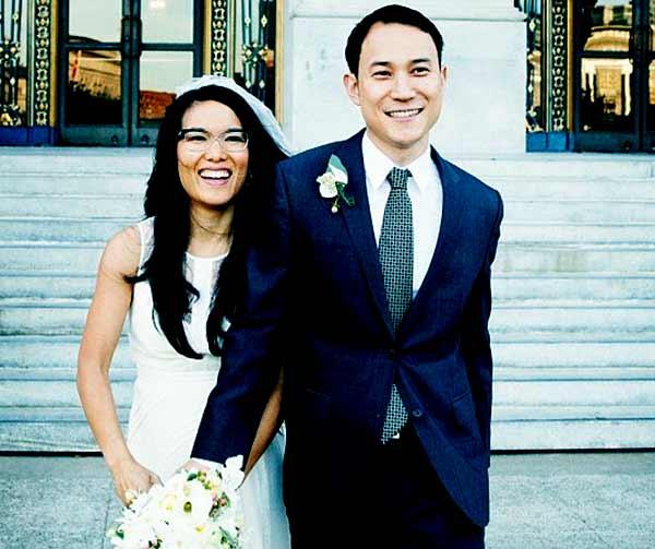Ali Wong wearing a wedding gown and holding a bouquet And Justin Hakuta wearing a three-piece suit at their wedding