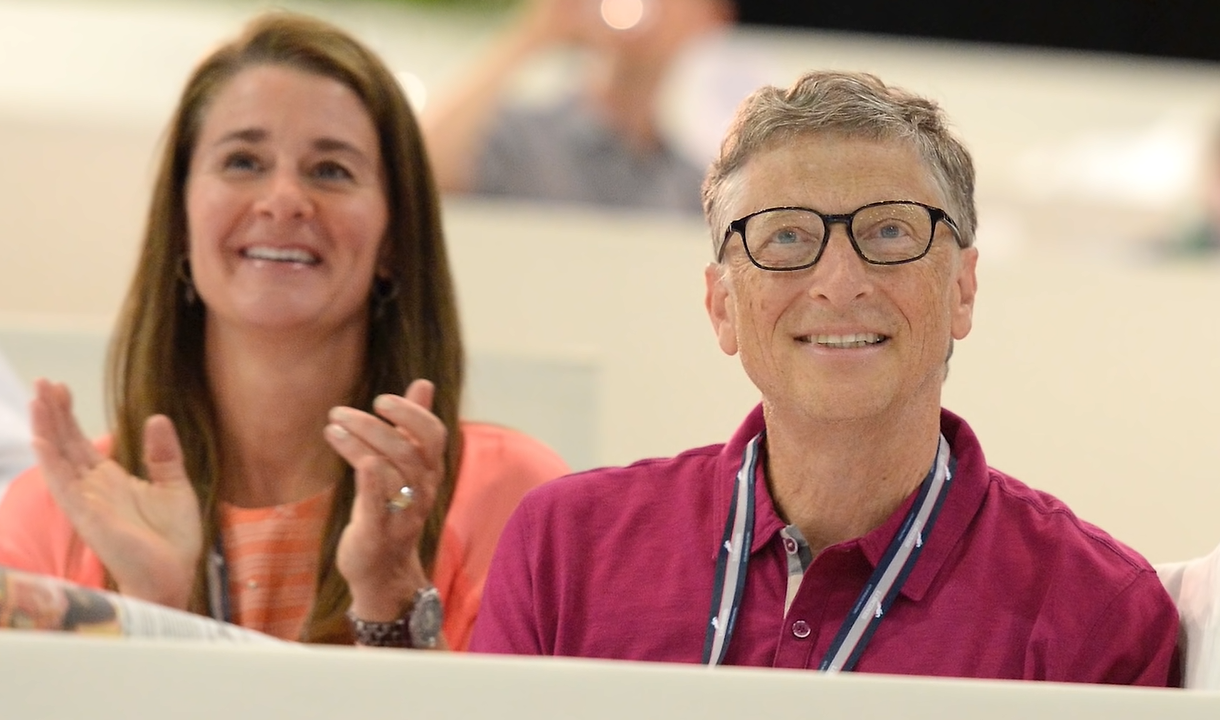 Bill Gates in maroon polo shirt and Melinda Gates in orange shirt about to clap