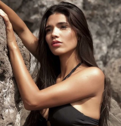 Paloma Jiménez wearing a black bikini while holding on to a rock formation for a modeling gig