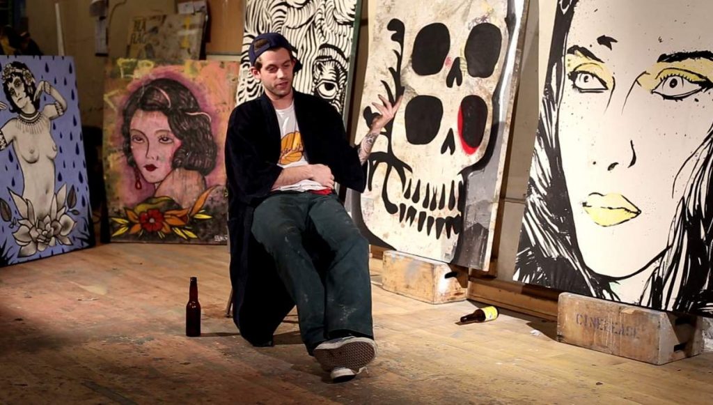 Spencer Elden sitting on a chair with paintings behind the scene