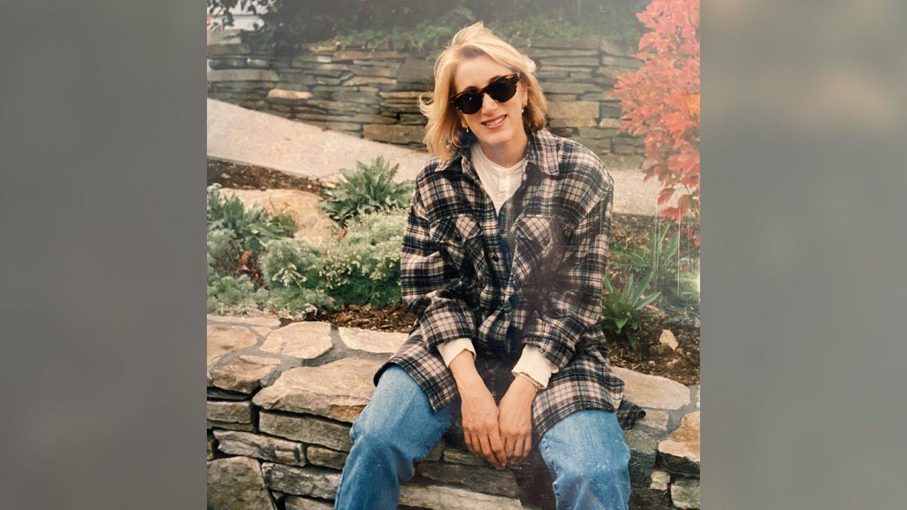 Denise Rosen wearing sunglasses sitting on a rocks wall