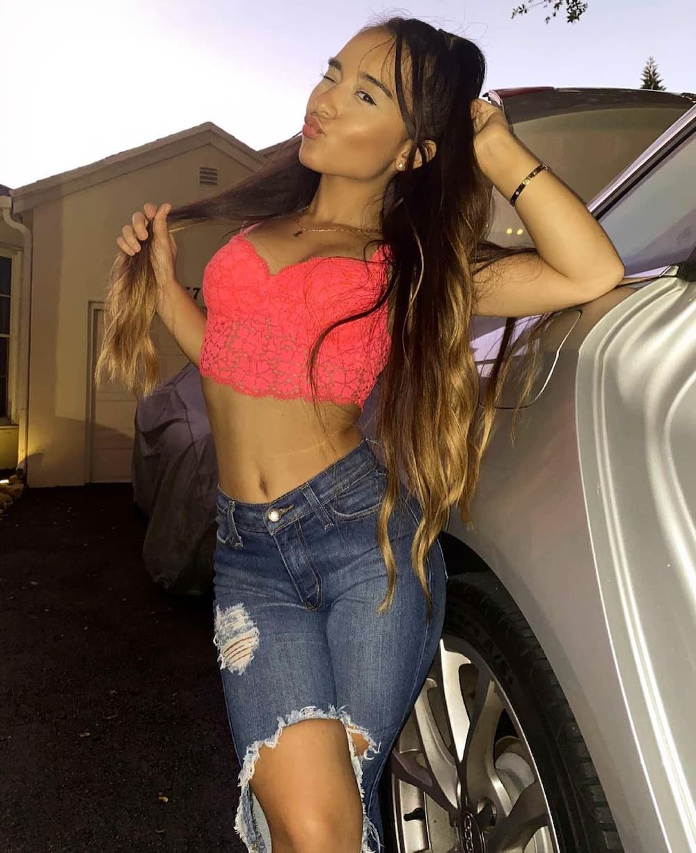Alahna Ly leaning on a car outside their house, wearing a neon pink bralette and tattered jeans