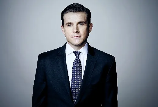 Phil Mattingly wearing a black suit and black and white stripe tie while posing on gray background