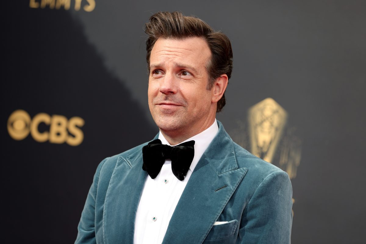 Jason Sudeiskis wearing a blue green coat and black bow while smiling