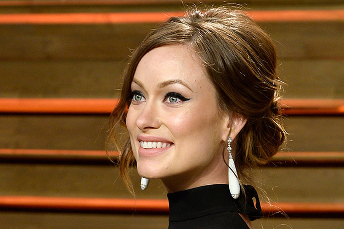 Olivia Wilde smiling in a black attire and large teardrop earrings