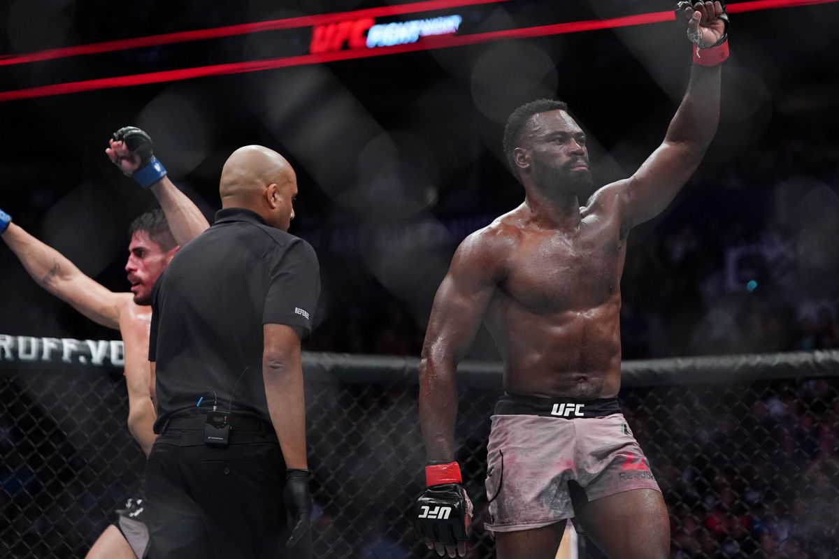 Uriah Hall raising his left arms, a referee, and another MMA fighter in the ring
