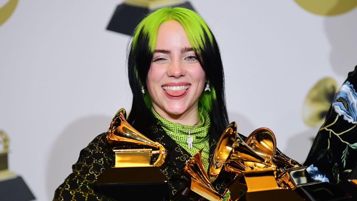 Billi Eilish sticking her tongue out while holding 5 grammy