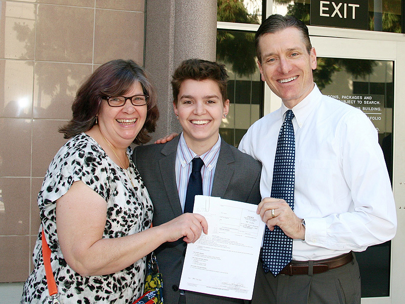 Elliot Fletcher standing with family wearing a coat and holding a paper