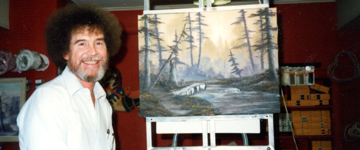 Bob Ross posing beside one of his thousands of paintings