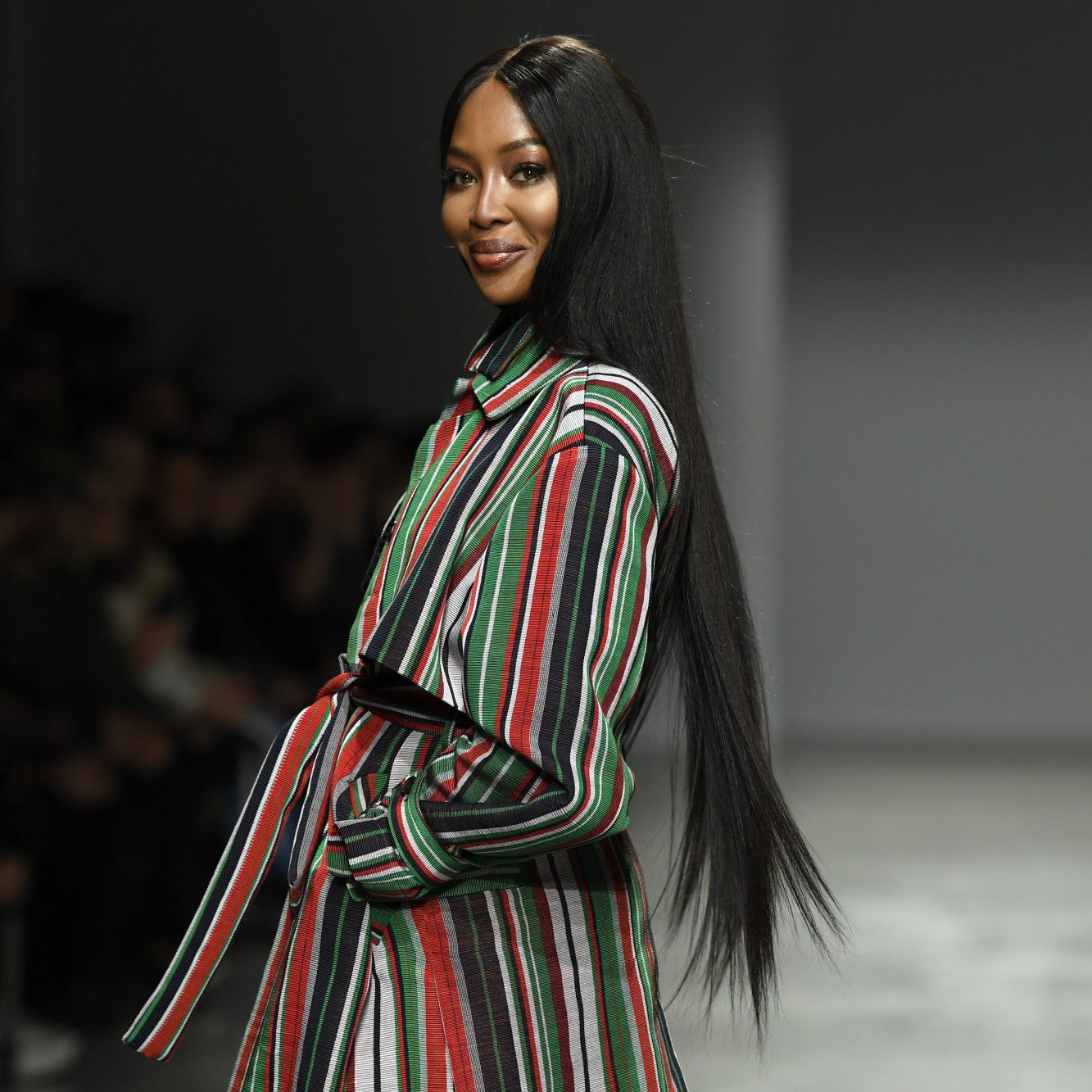 Naomi Campbell wearing a multi-colored striped dress and walking on ramp