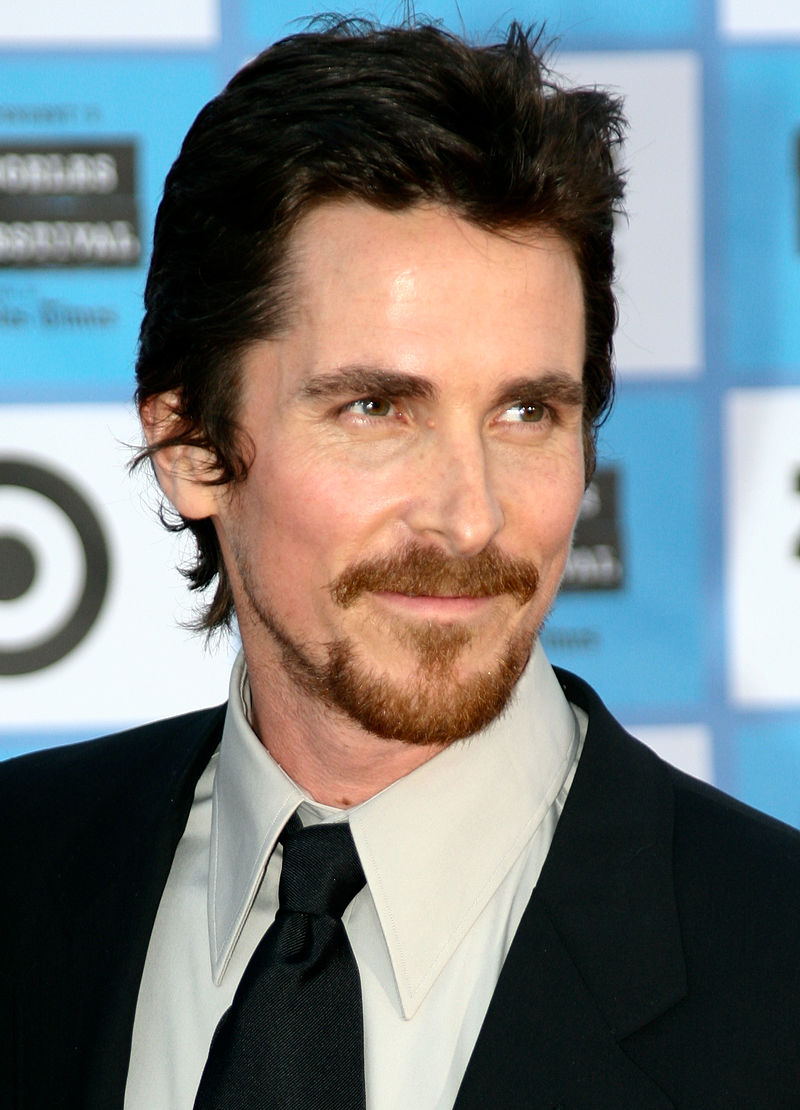 Christian Bale in messy hair wearing a black coat and tie