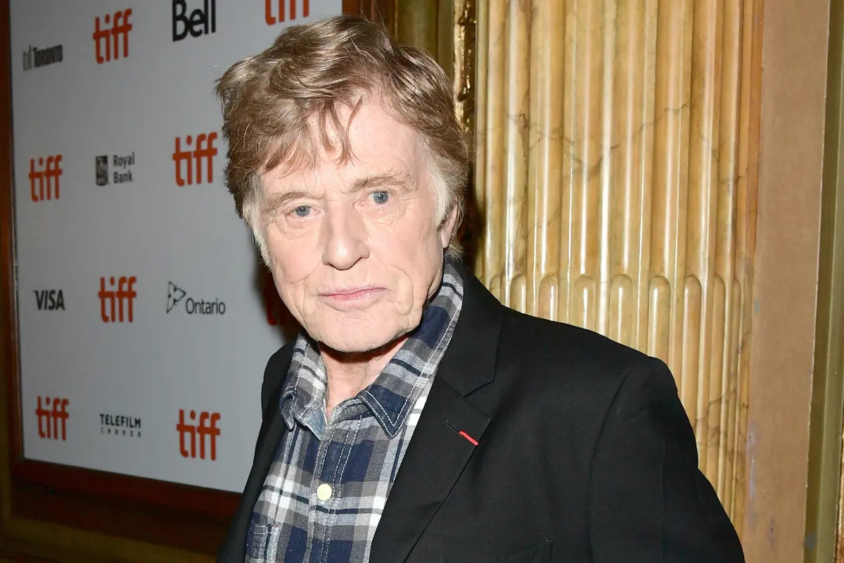 Robert Redford wearing a black suit and blue checkered polo