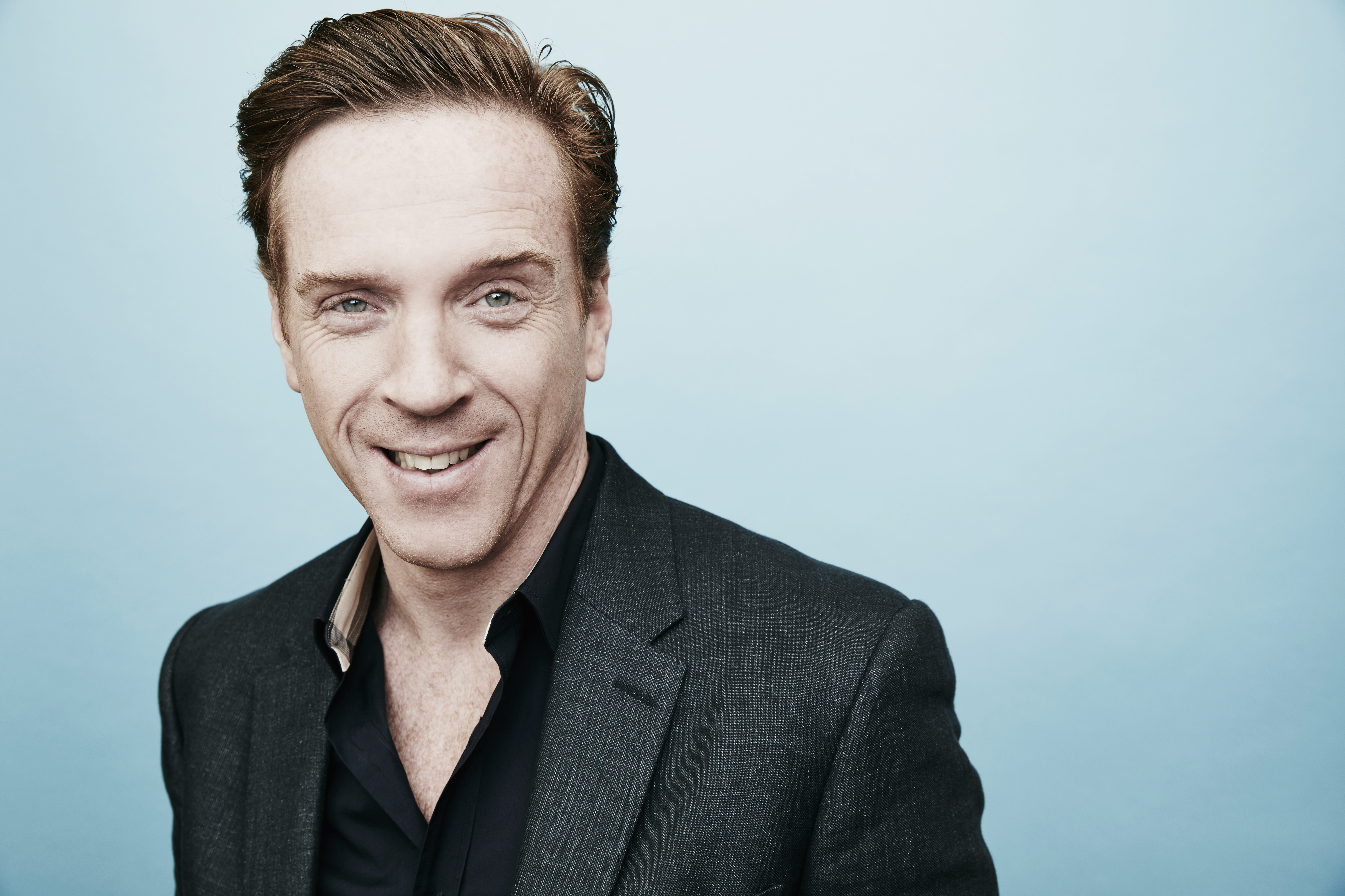 Damian Lewis in a coat smiling