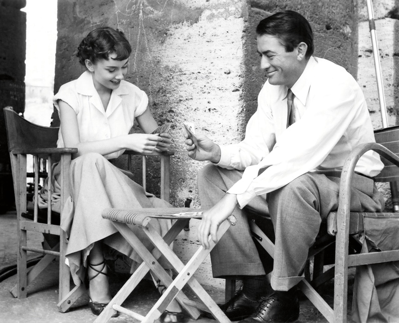 Gregory Peck smiling and playing cards with Audrey Hepburn