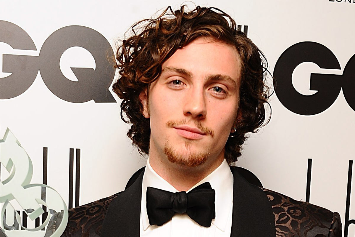 Aaron Taylor Johnson in a coat and black bow tie smiling