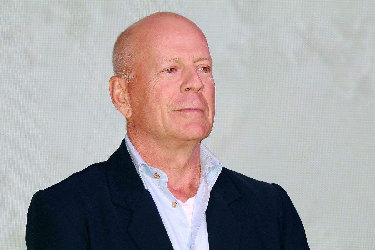 Smiling Bruce Willis in a black coat and blue long sleeves