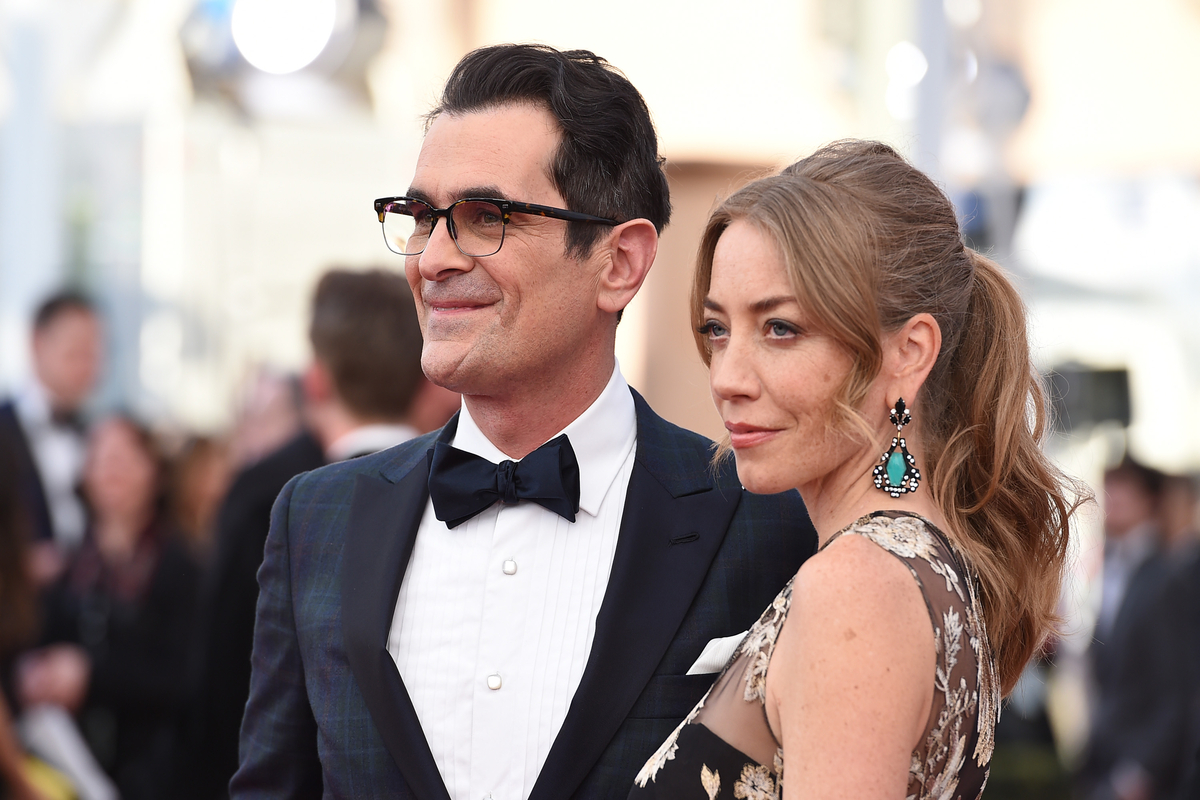 Ty Burrell in a black coat and and black bow tie with eye glasses and Holly Burrell smiling in a floral black see throuh attire