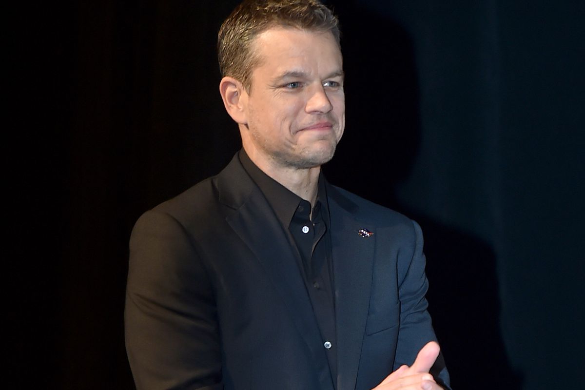 Matt Damon in a black suit while smiling and clapping his hands