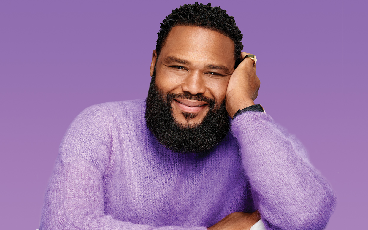 Anthony Anderson Is Wearing A Lilac Sweater, A Black Wrist Watch, And A Gold Ring On His Little Finger