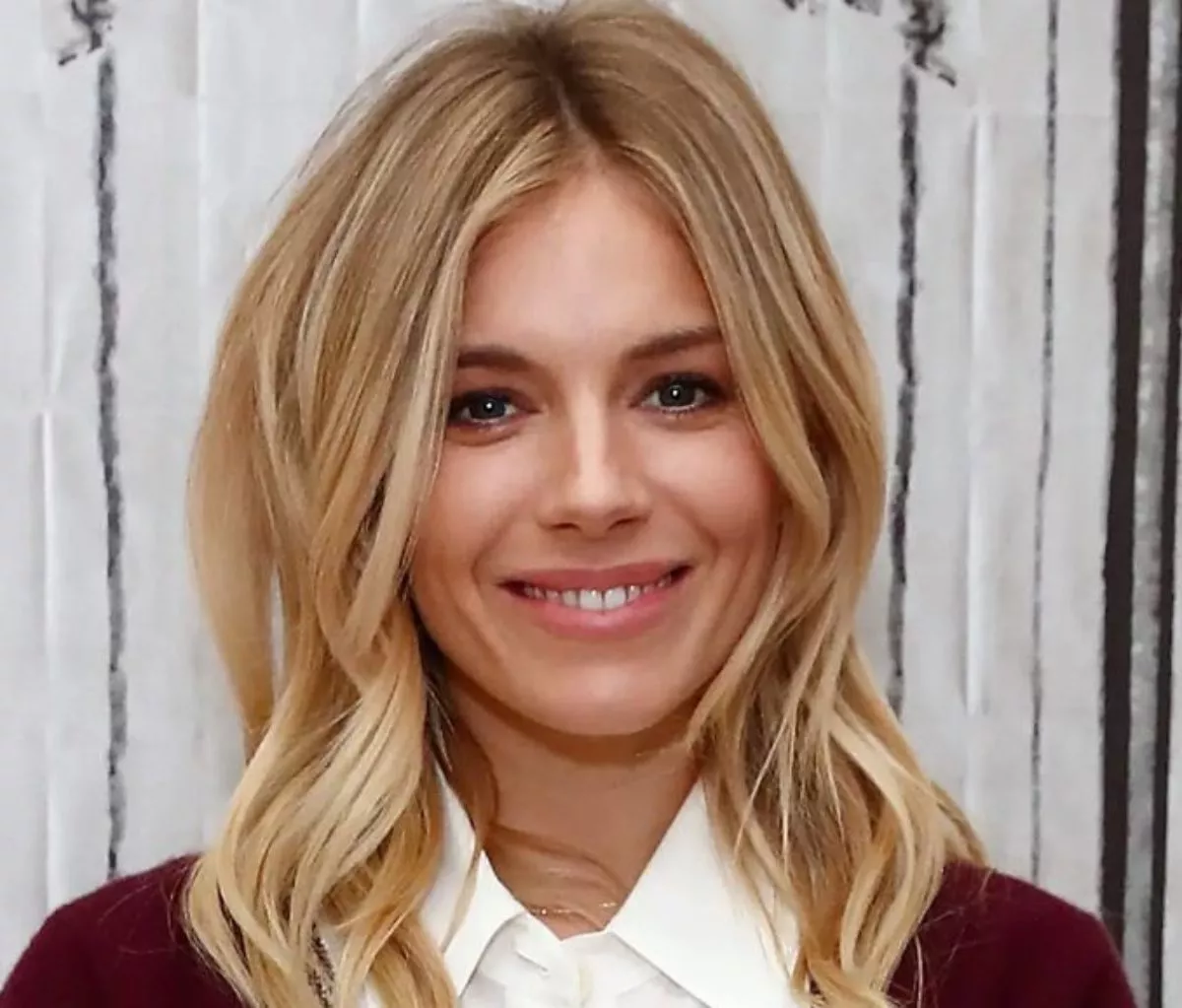 Sienna Miller wearing her blonde hair down and red and white top while smiling