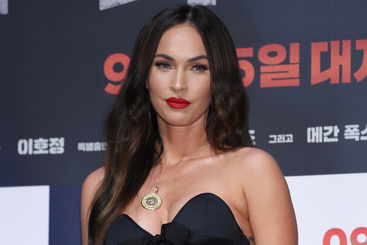 Megan Fox in a red lipstick, black dress, and a necklace with a gold round pendant