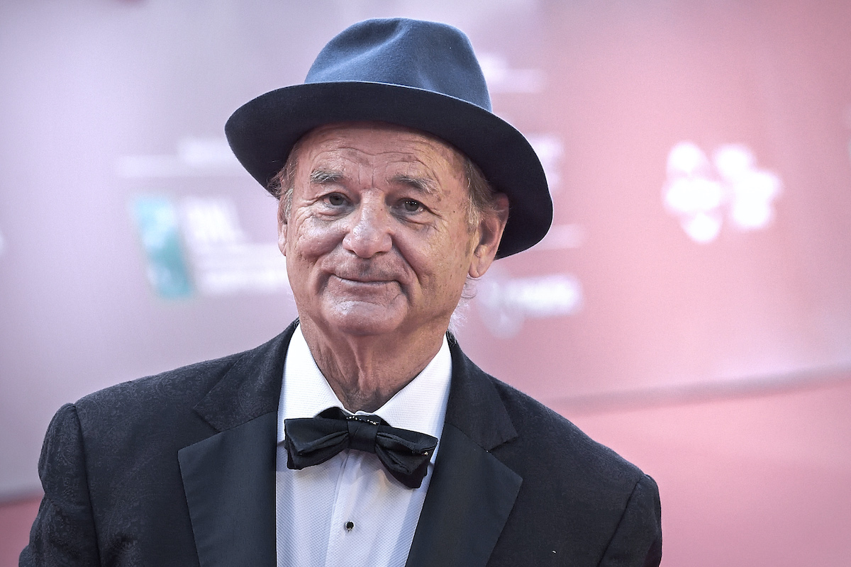 Smiling Bill Murray wearing a black hat, black suit, and black bow tie