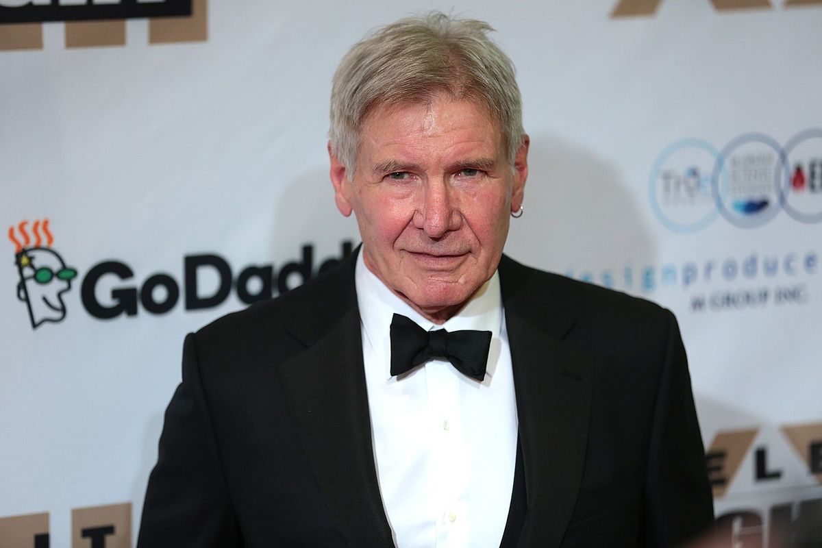Harrison Ford smiling wearing a suit and black bow tie with earring in his left ear