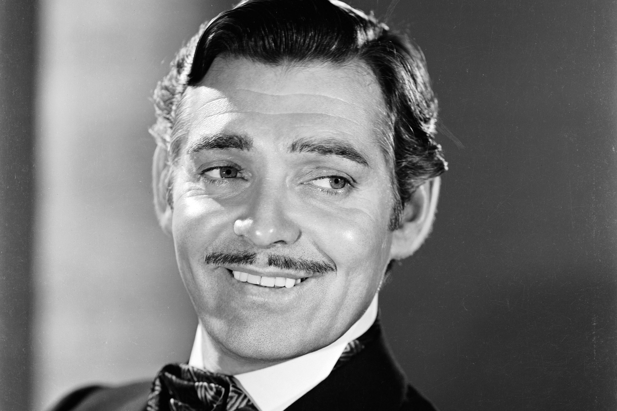 Smiling Clark Gable with a mustache in a suit and brushed up hair 
