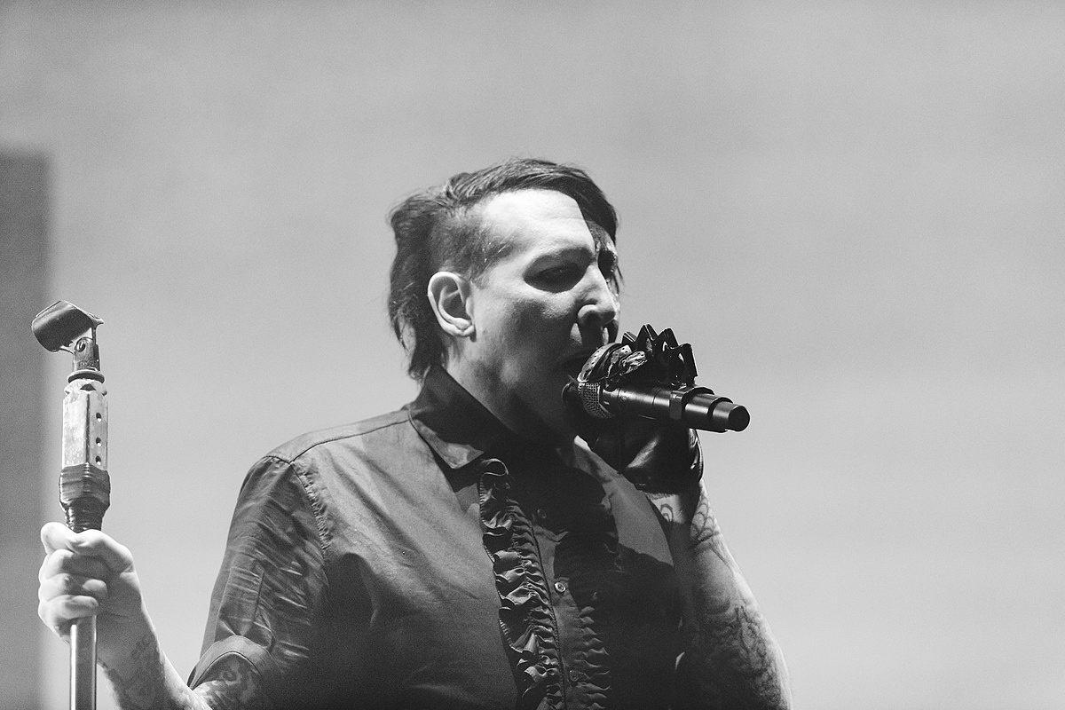 Marilyn Manson holding a mic and microphone stand while wearing a polo