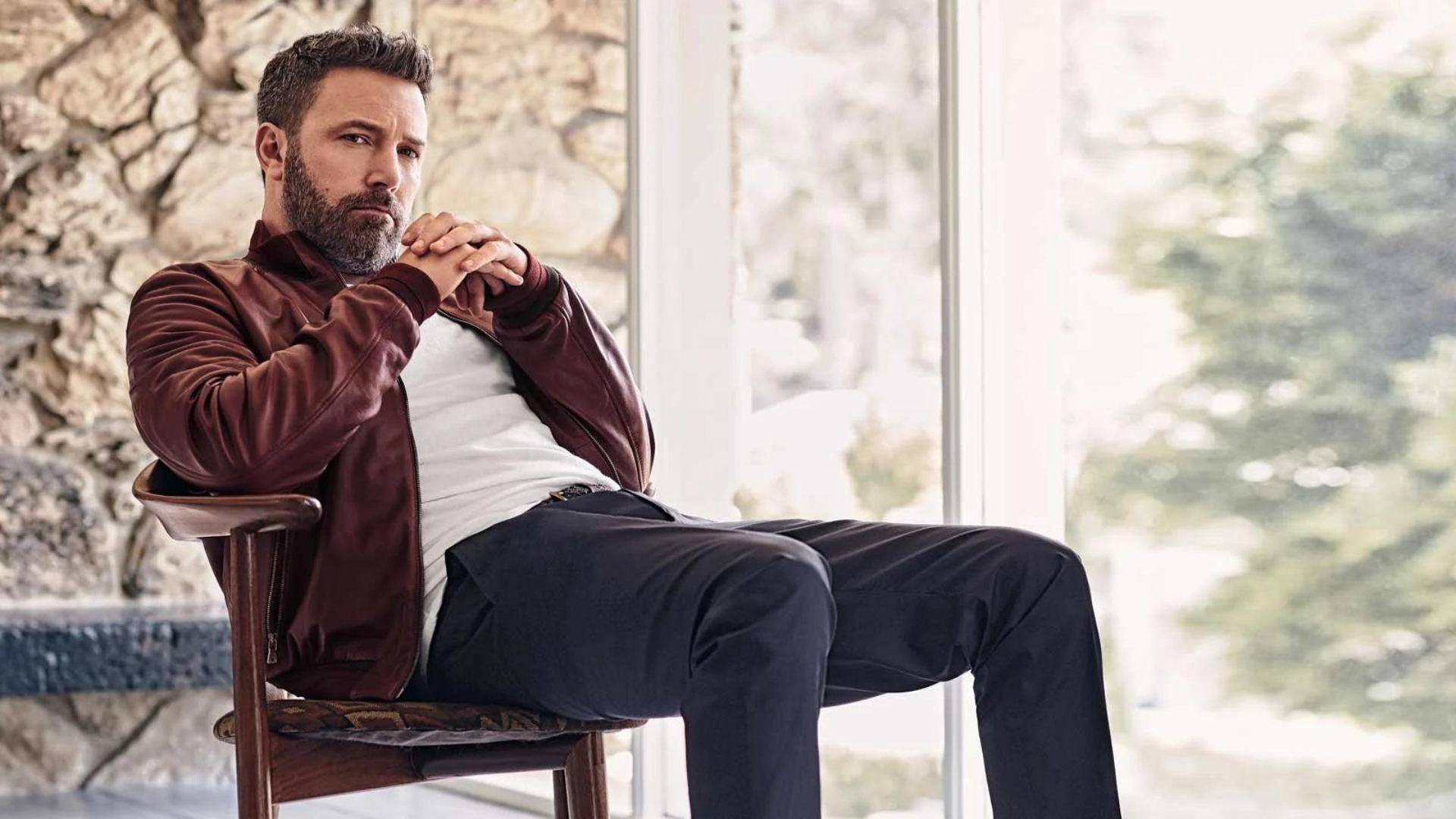 Serious looking Ben Affleck sitting on the wooden chair 