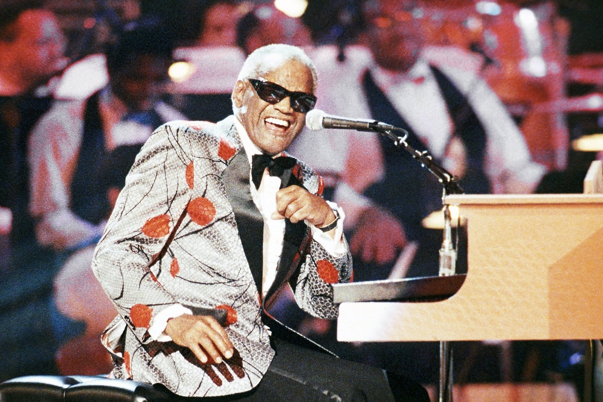 Ray Charles smiling while singing and a piano in front of him