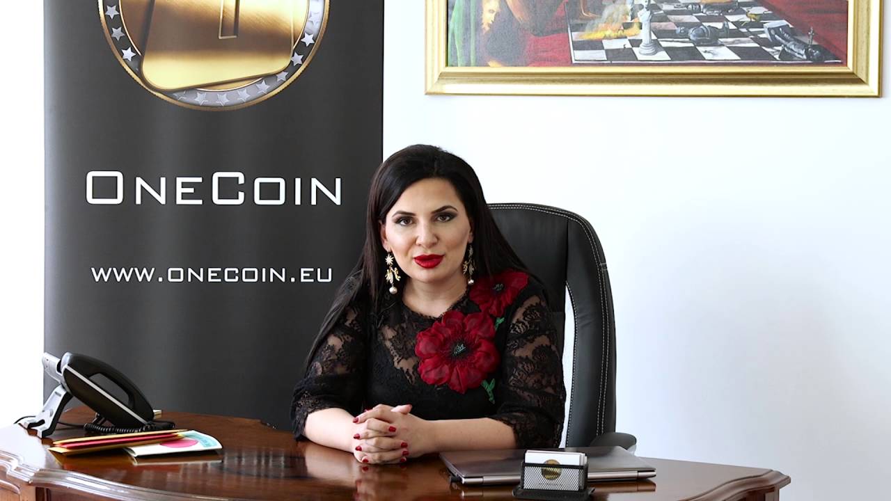 Ruja Ignatova wearing a black top with red big flowers and red lipstick sitting in a chair