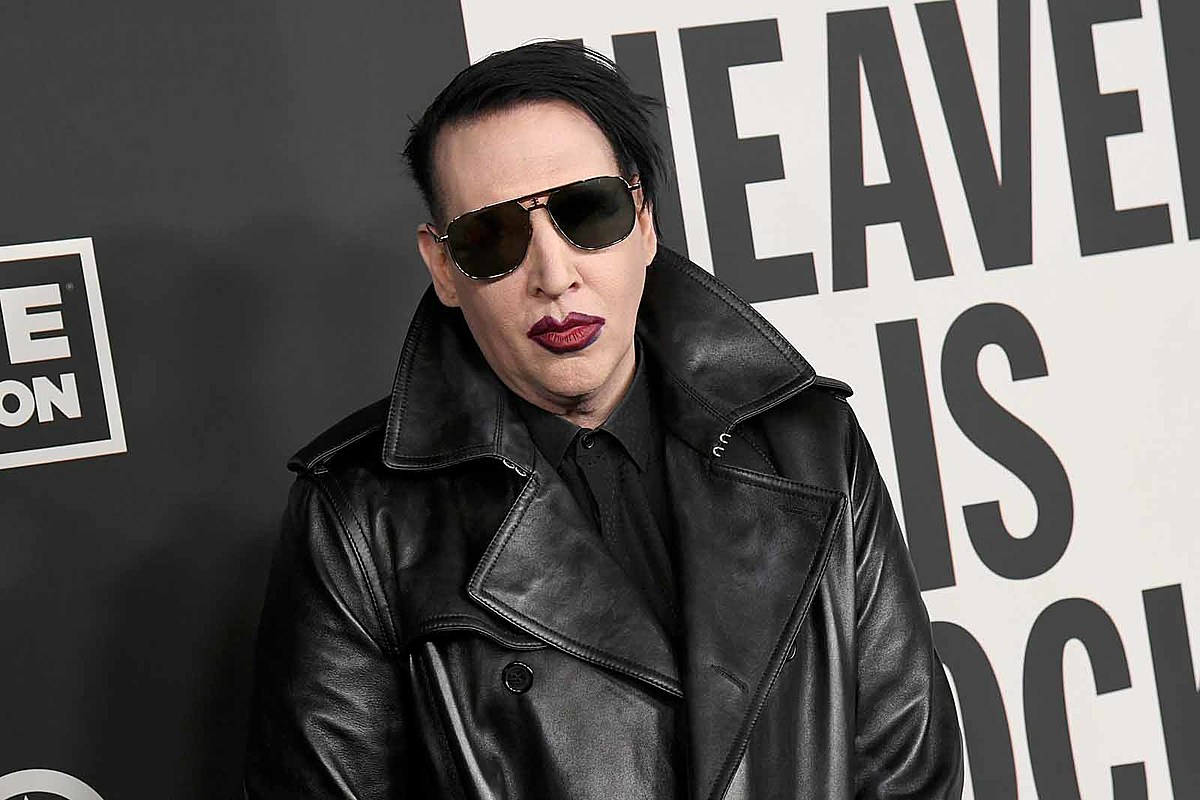 Marilyn Manson wearing a black leather jacket, black sunglasses, and maroon lipstick