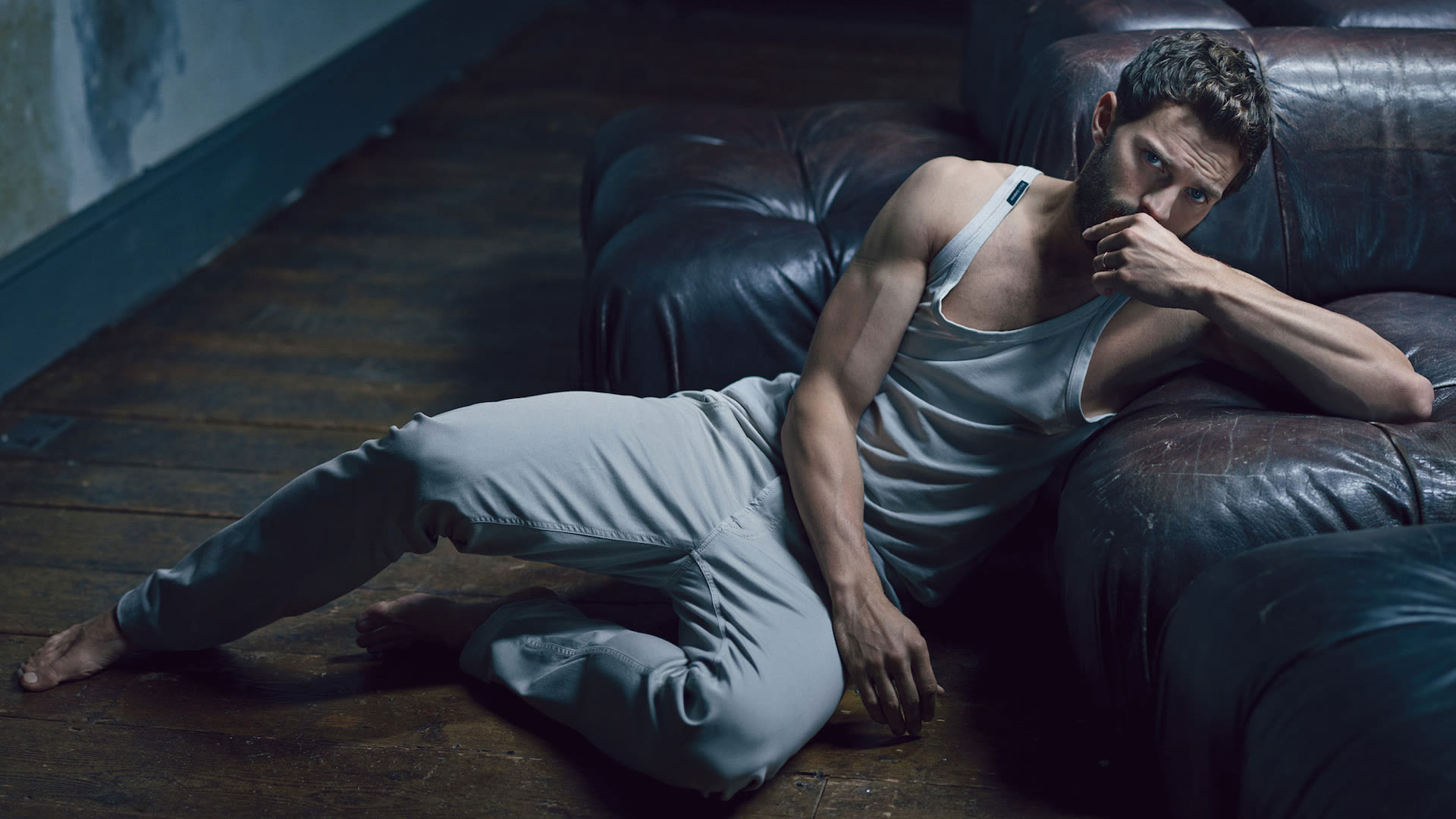 Jamie Dornan sitting on the floor while leaning on the couch
