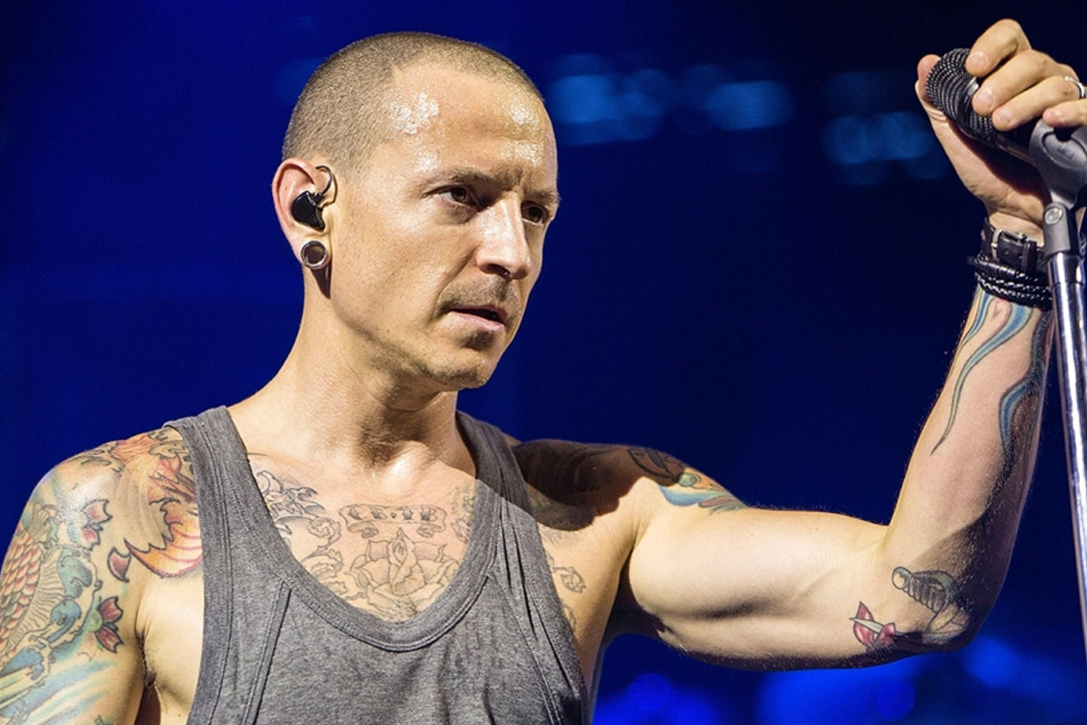 Chester Bennington wearing a gray tank top and holding a microphone with a stand