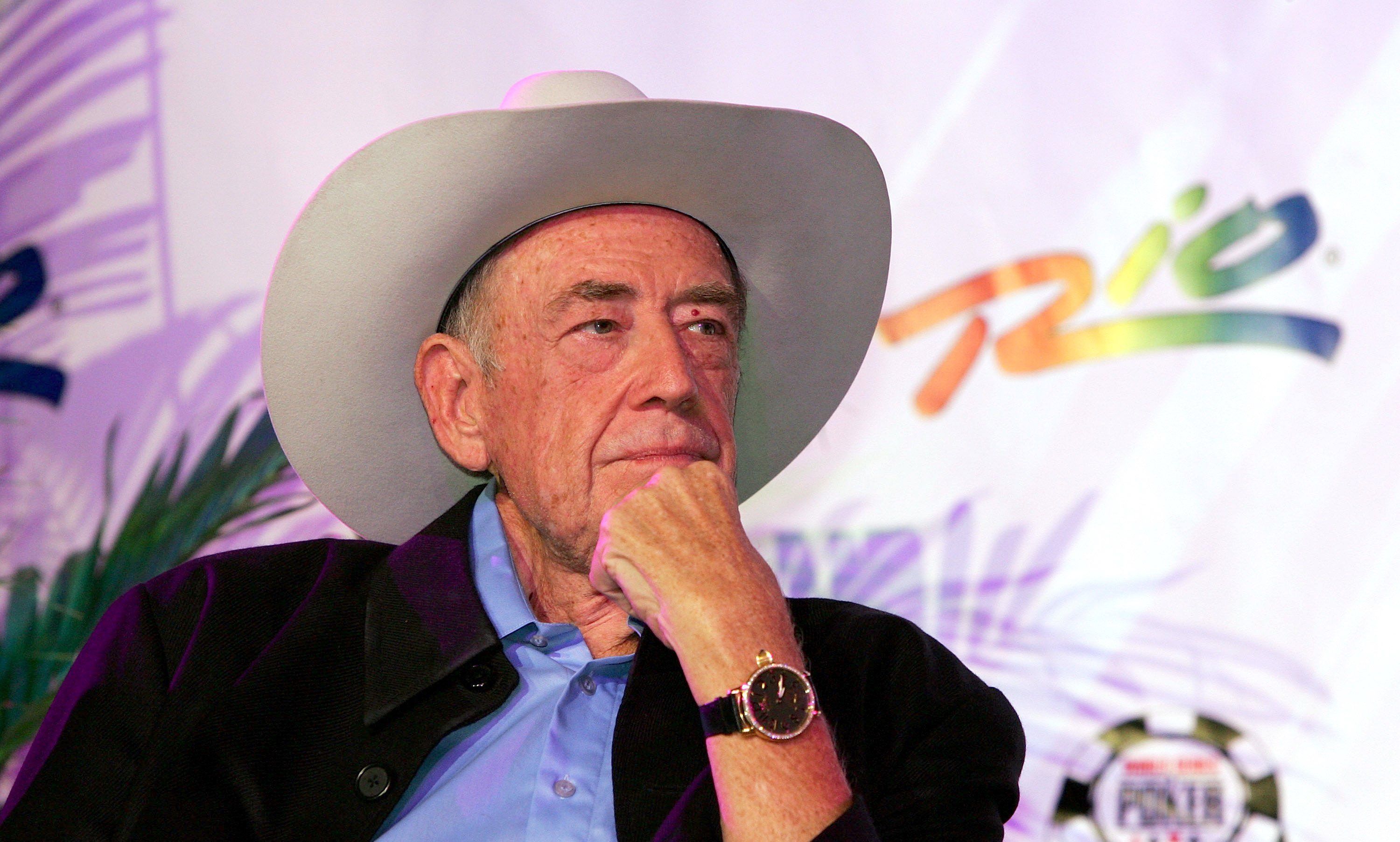 Doyle Brunson wearing a blue polo shirt, black coat, a watch, and a white hat