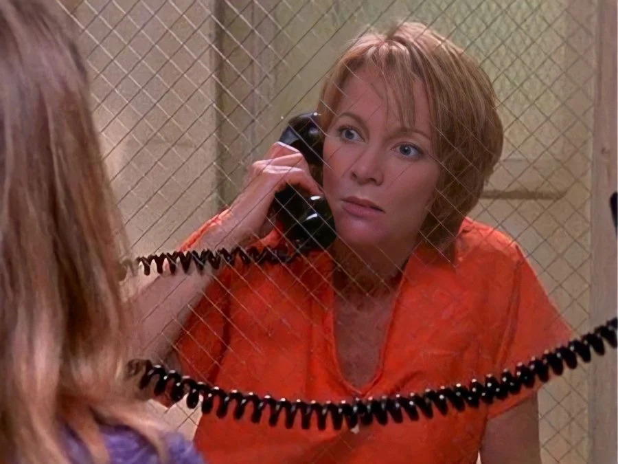 Mary Mara as one of her TV series character wearing an orange prisoner uniform while holding a telephone