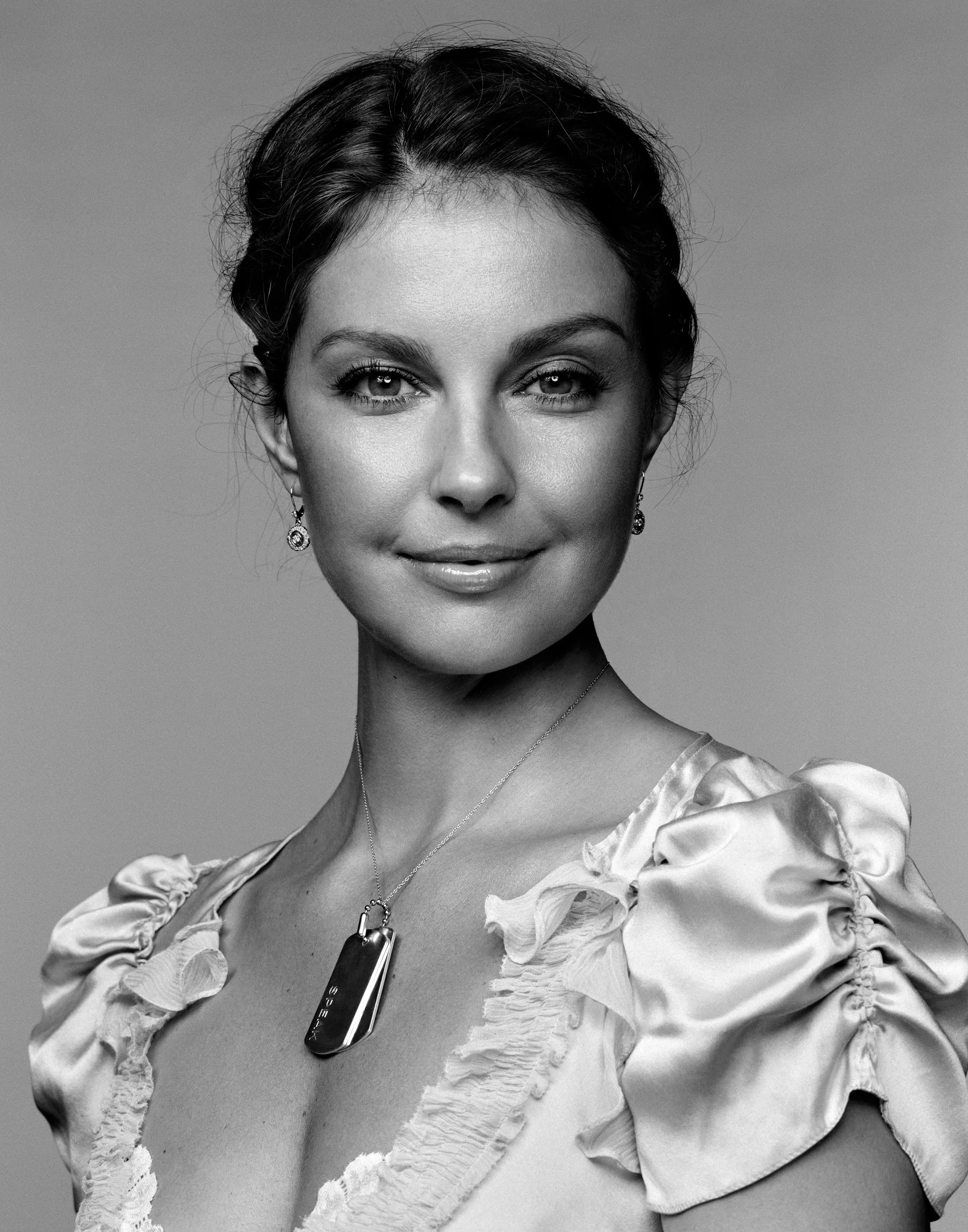 A headshot of Ashley Judd wearing a dress and a dog tag necklace