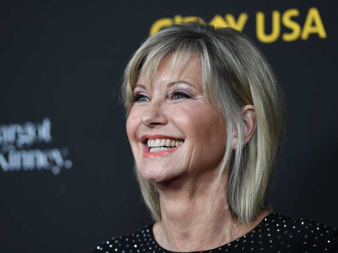 Olivia Newton-John smiling and wearing black outfit