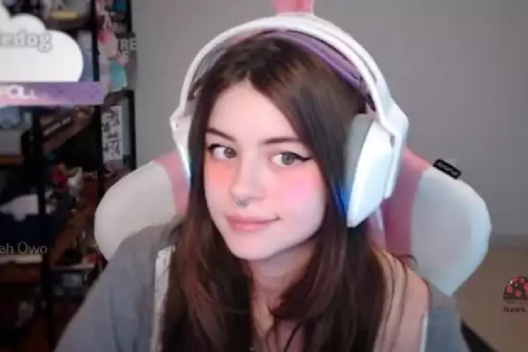 Hannah Owo is wearing headphones and sitting on a pink and white gaming chair during her Twitch live stream