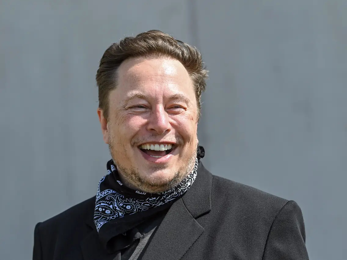 Elon Musk wearing a black coat and laughing