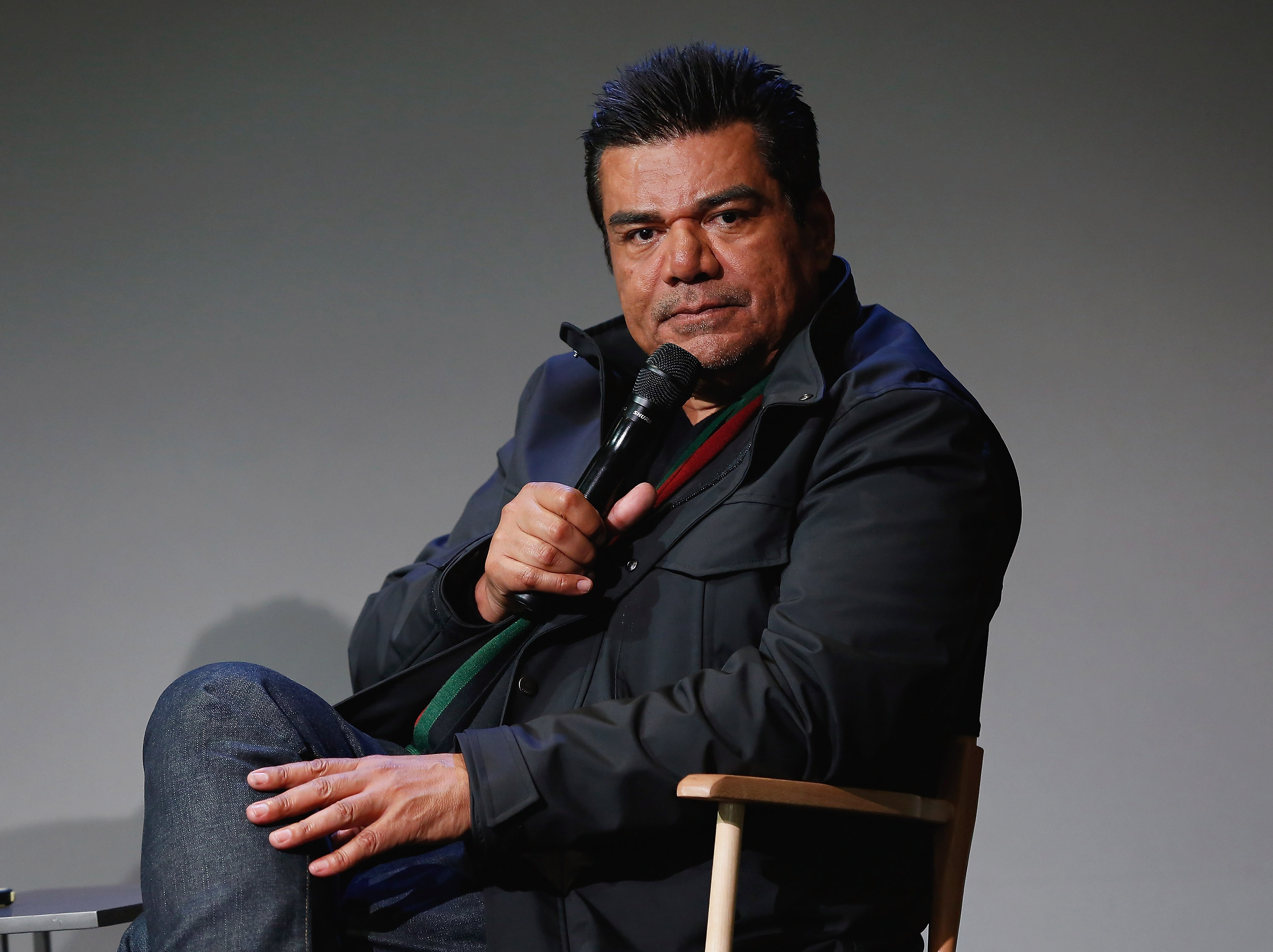 George Lopez holding a mic an sitting on a chair