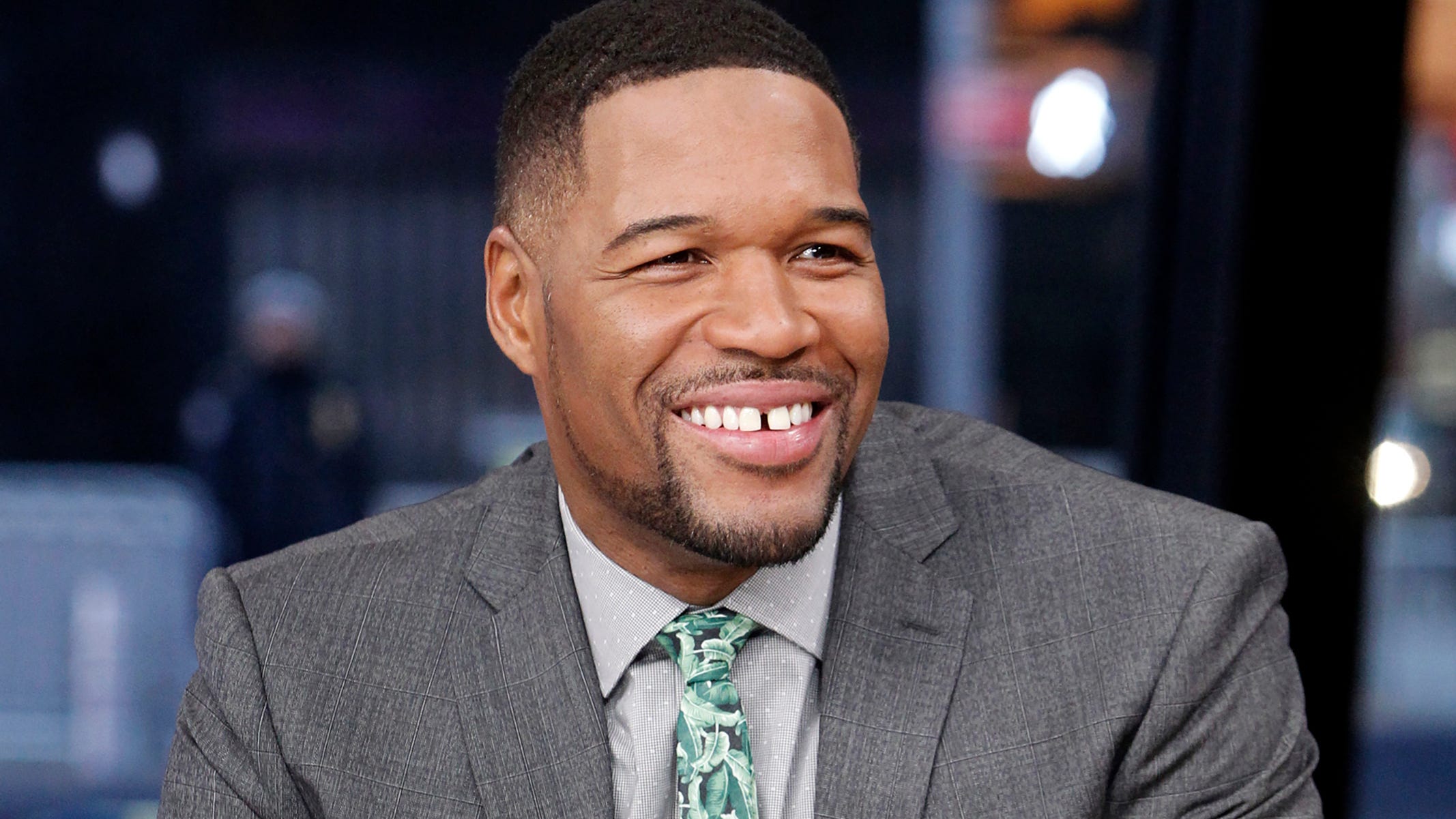 Smiling Michael Strahan wearing a gray suit