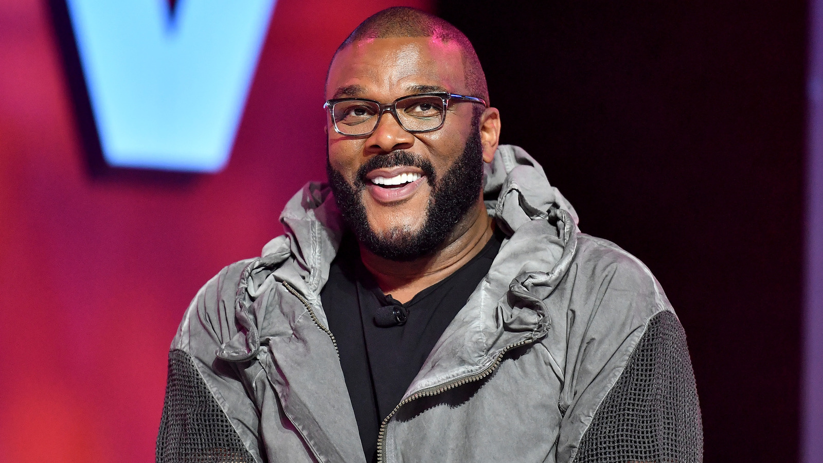 Smiling Tyler Perry wearing a gray jacket and eyeglasses